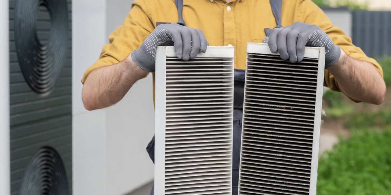 Plumber with gloves showing two heavily clogged air filters from a home air conditioning system.