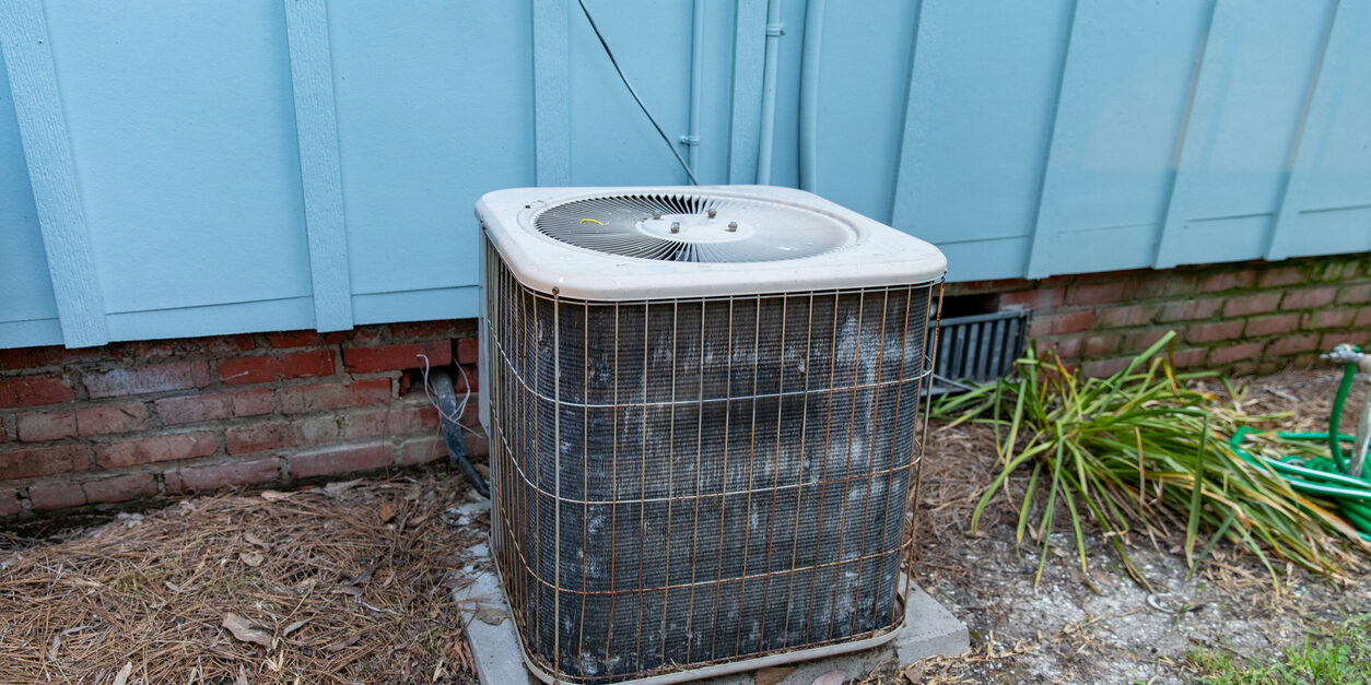 Old reusted air conditioner compresor sitting next to blue house Is it time to get a new HVAC?